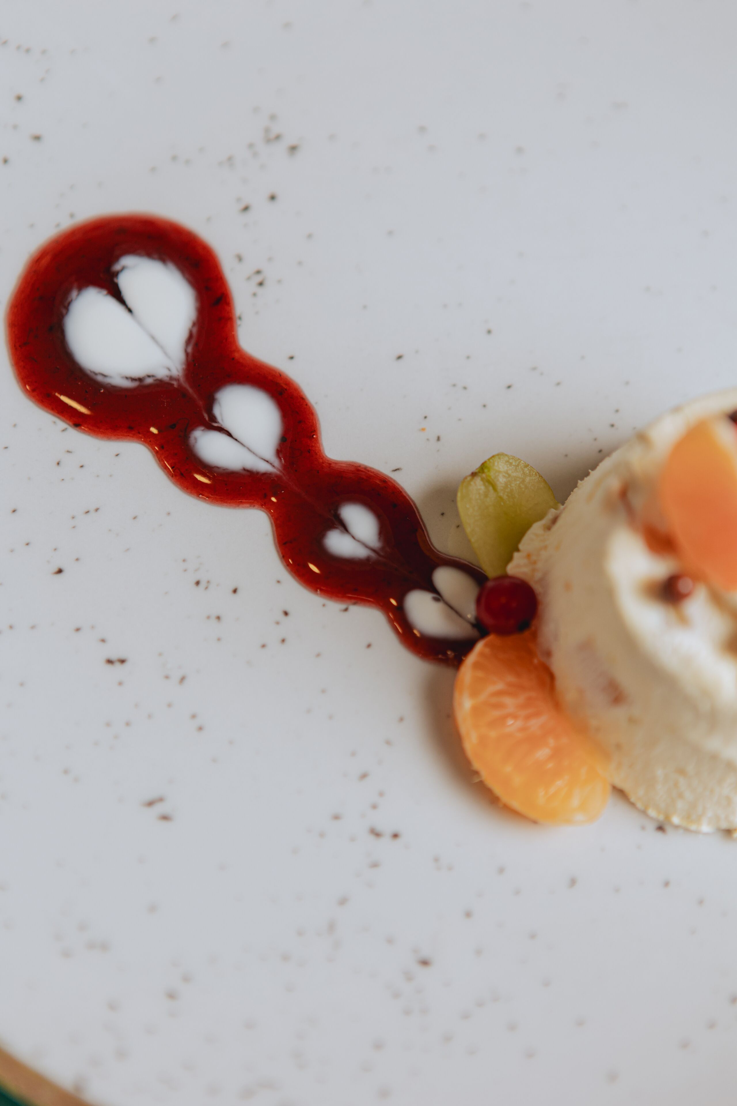 Un dessert composé d’une base blanche, d’une tranche d’orange et d’une sauce rouge, le tout présenté sur une assiette blanche.