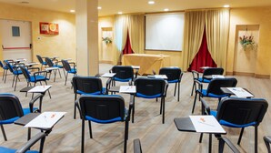 A conference room with rows of chairs, tables, a projector screen, and a red curtain. - Hotel Amico (Citta Sant'Angelo)