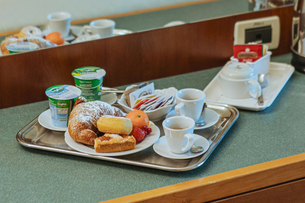 A hotel room with a neatly made bed, a tray with breakfast items, and a coffee maker on the nightstand.