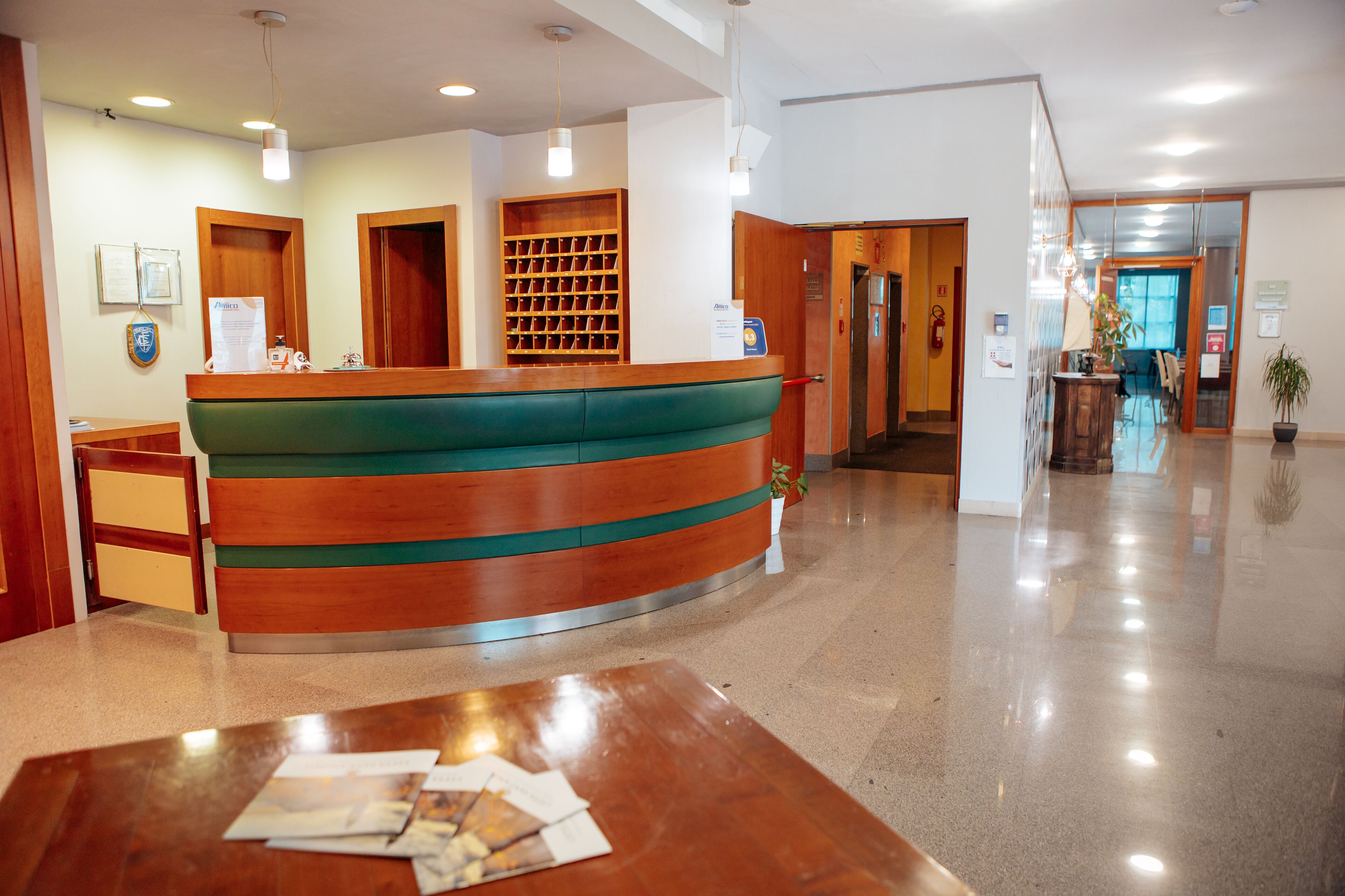 Zona de recepción con un mostrador de madera curvada, un escritorio y un área de espera con una mesa.