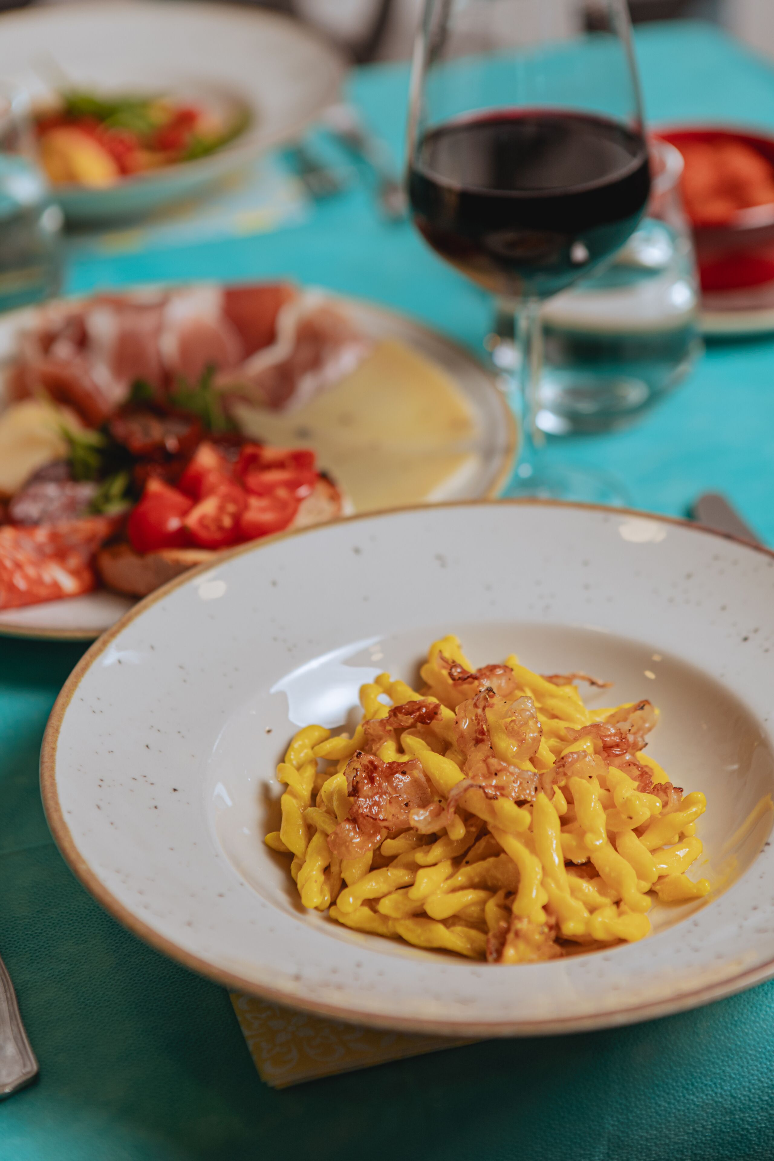 Une table à manger avec une assiette de pâtes, un verre de vin rouge et d’autres plats.