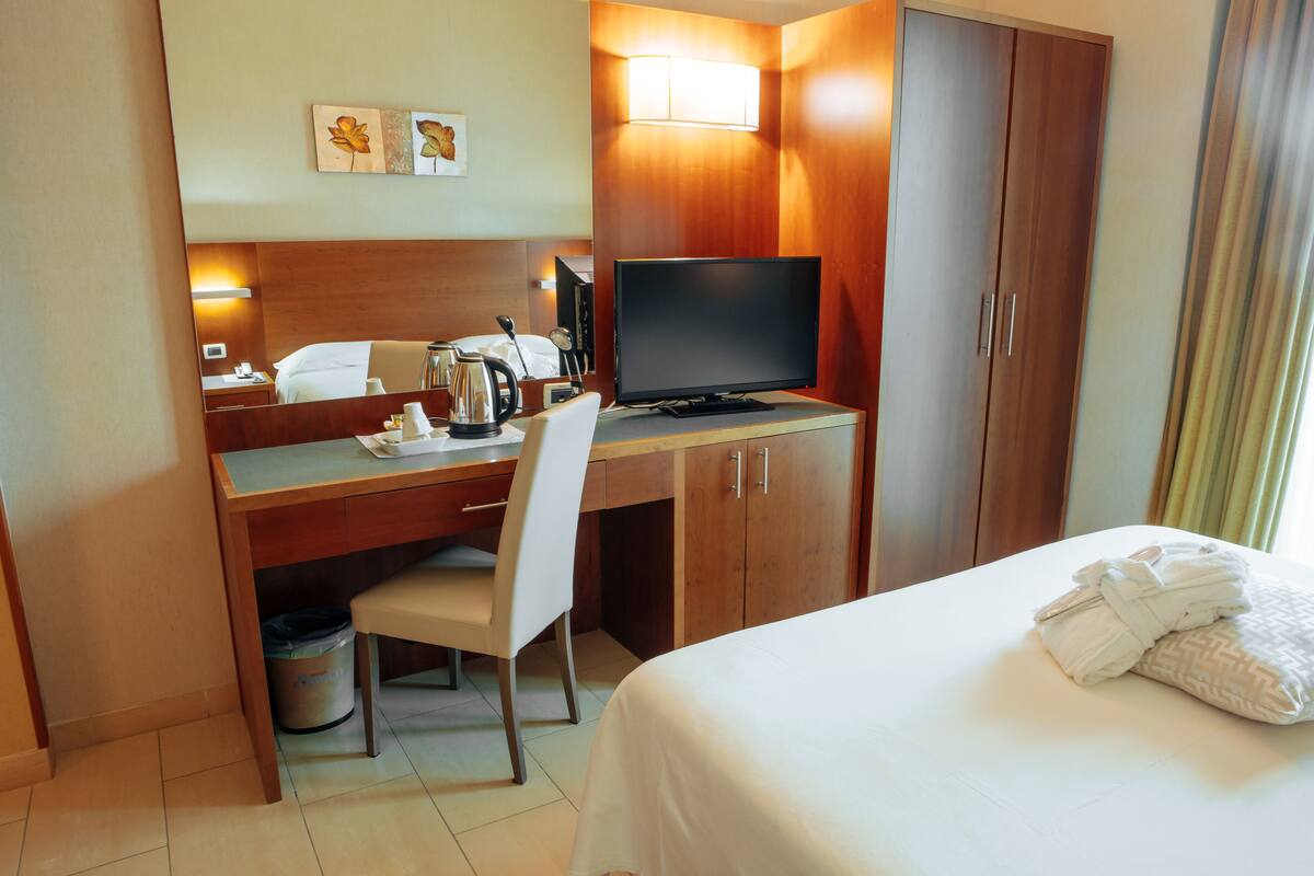 A hotel room with a bed, a desk with a computer, a chair, a television, and a wardrobe.