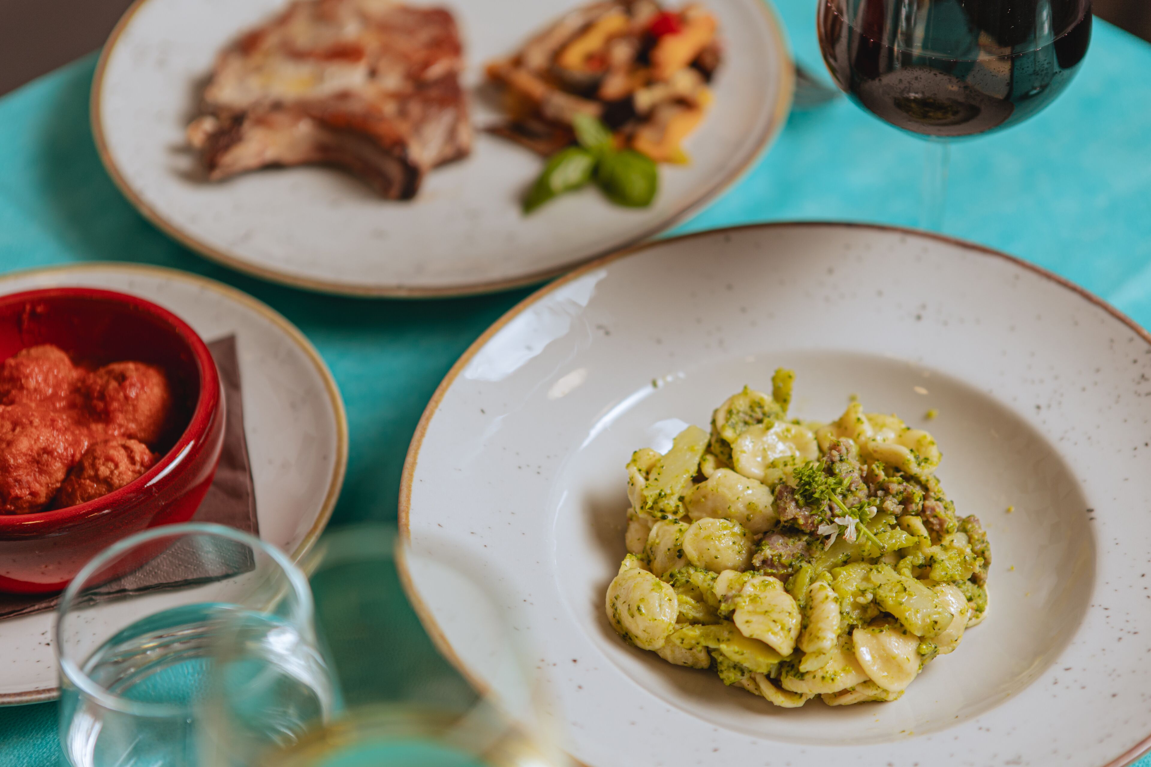 A table with three plates of food, a glass of wine, and a bowl of red sauce.