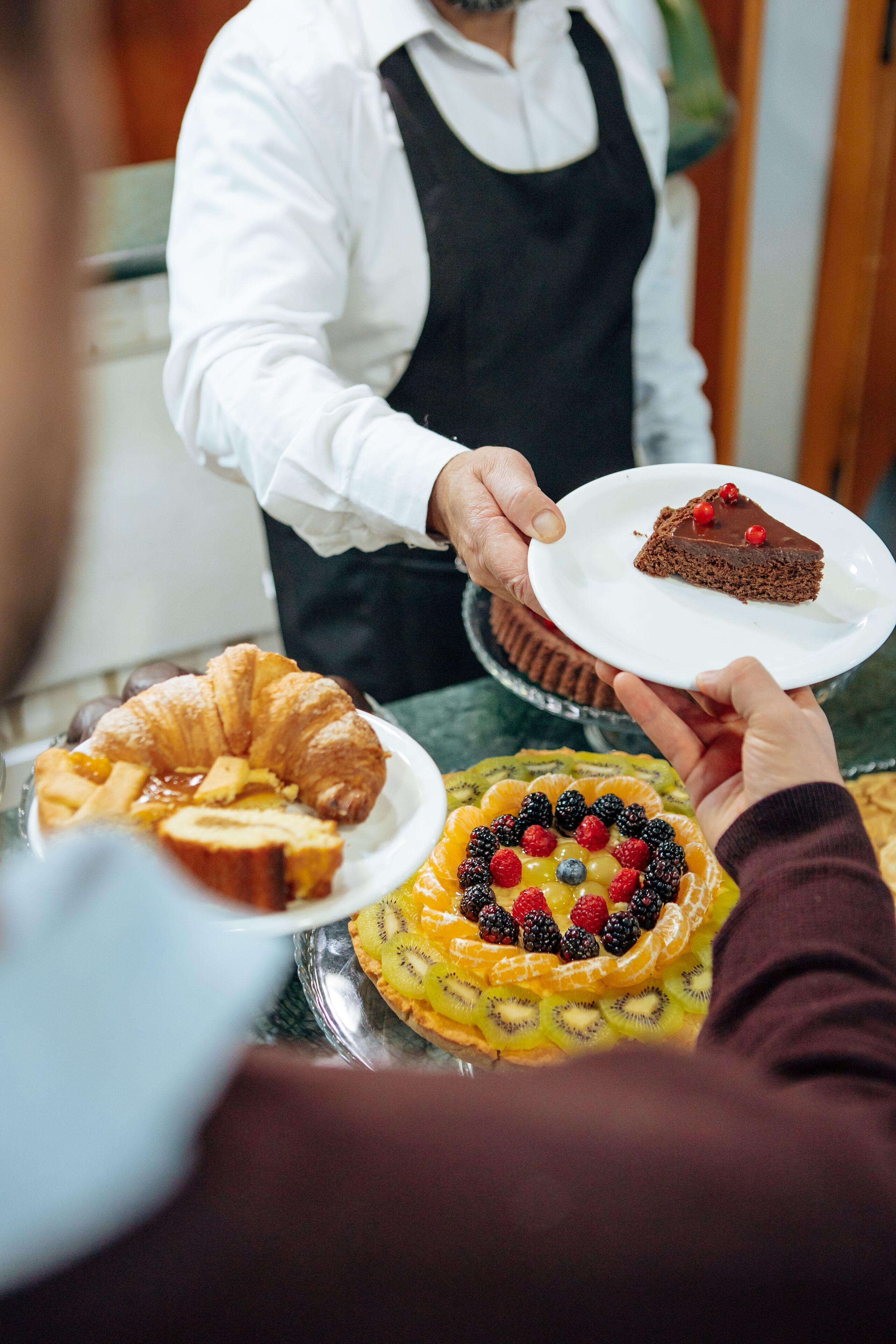 Une personne qui présente une part de gâteau au chocolat sur une assiette blanche.
