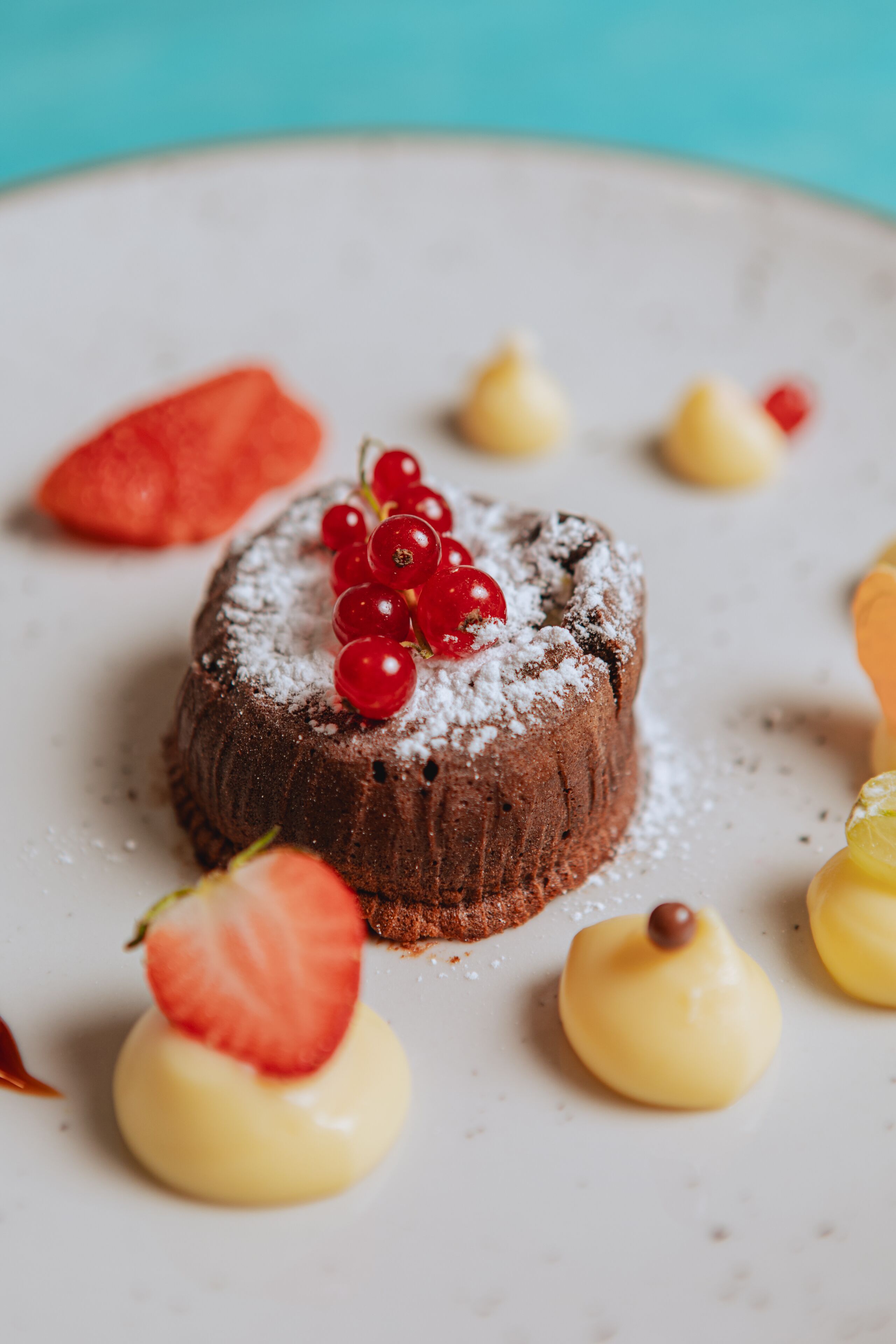 A dessert with a chocolate base, red berries, and yellow cream on a white plate.