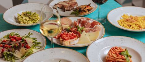 Una mesa con varios platos de comida, incluyendo pasta, ensaladas y carnes, además de dos copas de vino.