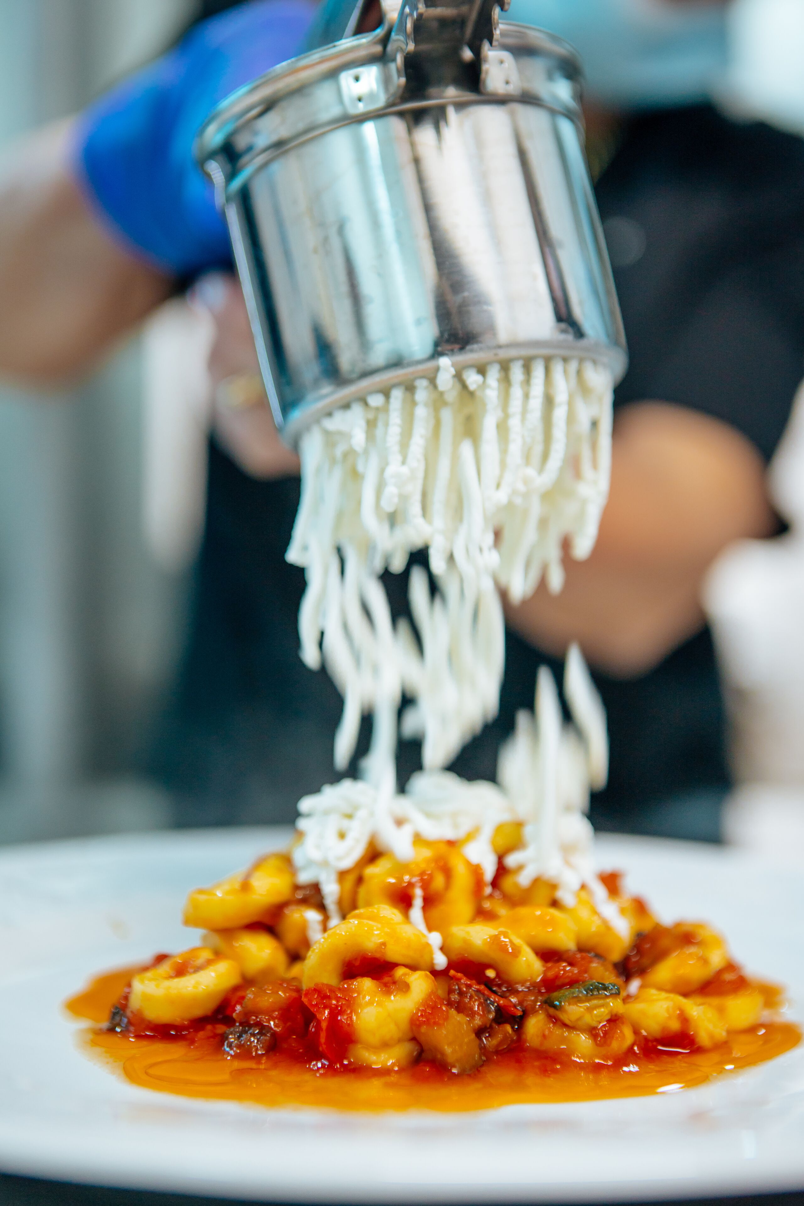 A person pouring white noodles over a plate of pasta with tomato sauce.