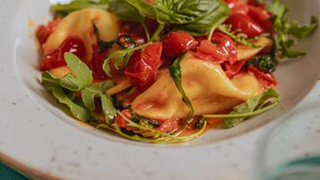 Ein Teller Ravioli mit Tomatensauce und Grünzeug.