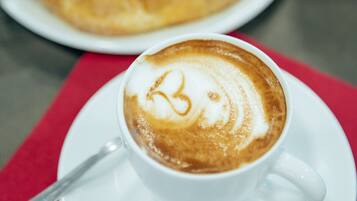 Una taza de café con arte de latte sobre un plato, un plato con croissants y un mantel individual rojo sobre una mesa.