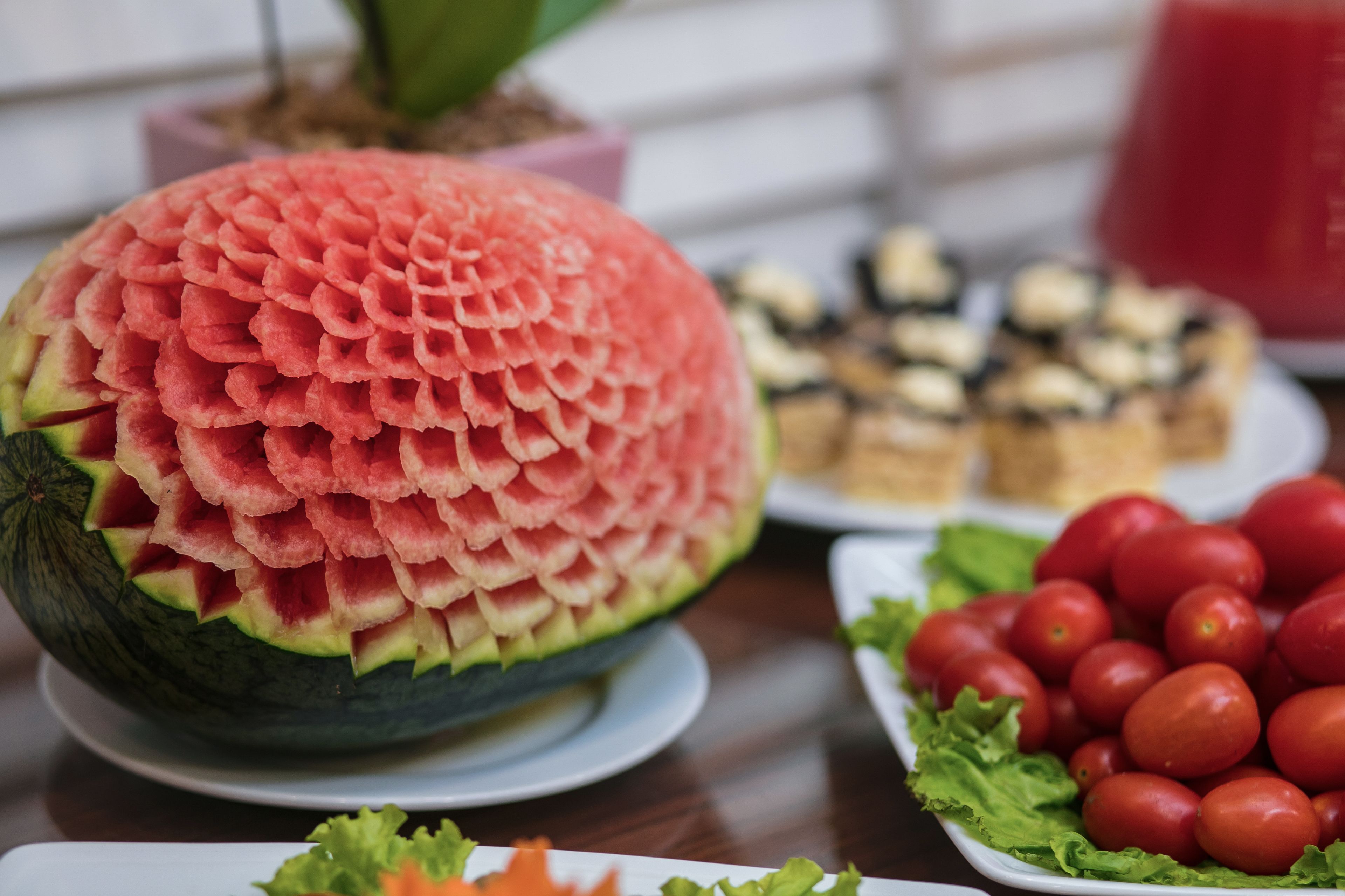 A table with a carved watermelon centerpiece, a plate of cherry tomatoes, and a plate of food.