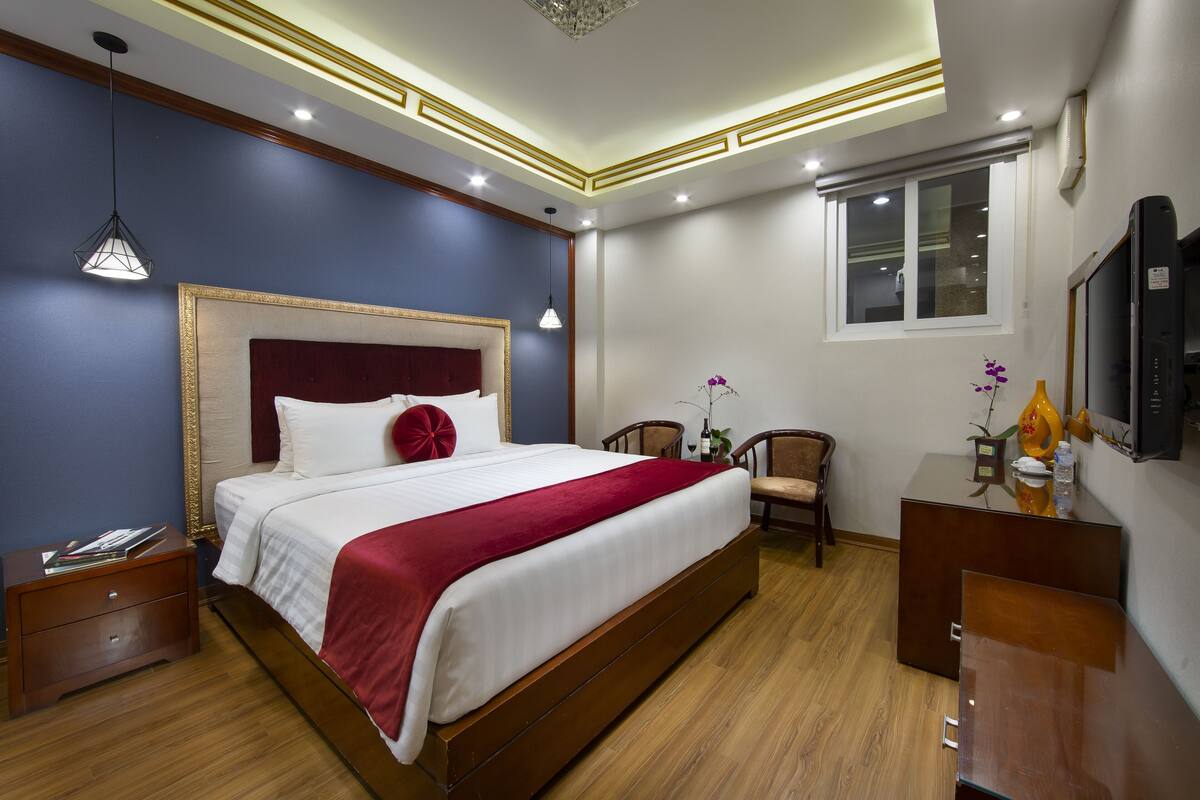 Une chambre d’hôtel avec un grand lit, une table de chevet en bois et un bureau avec une chaise.