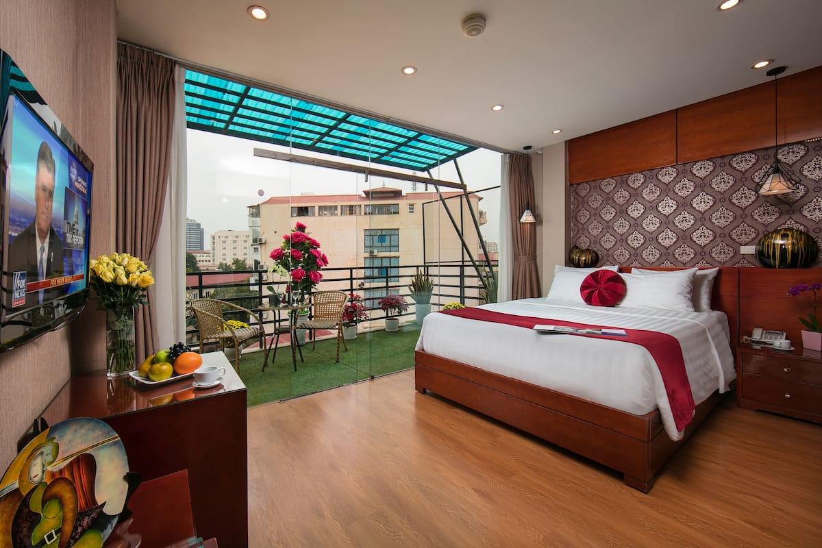Une chambre d’hôtel avec un grand lit, un bureau avec un ordinateur, une télévision et un balcon offrant une vue sur la ville.
