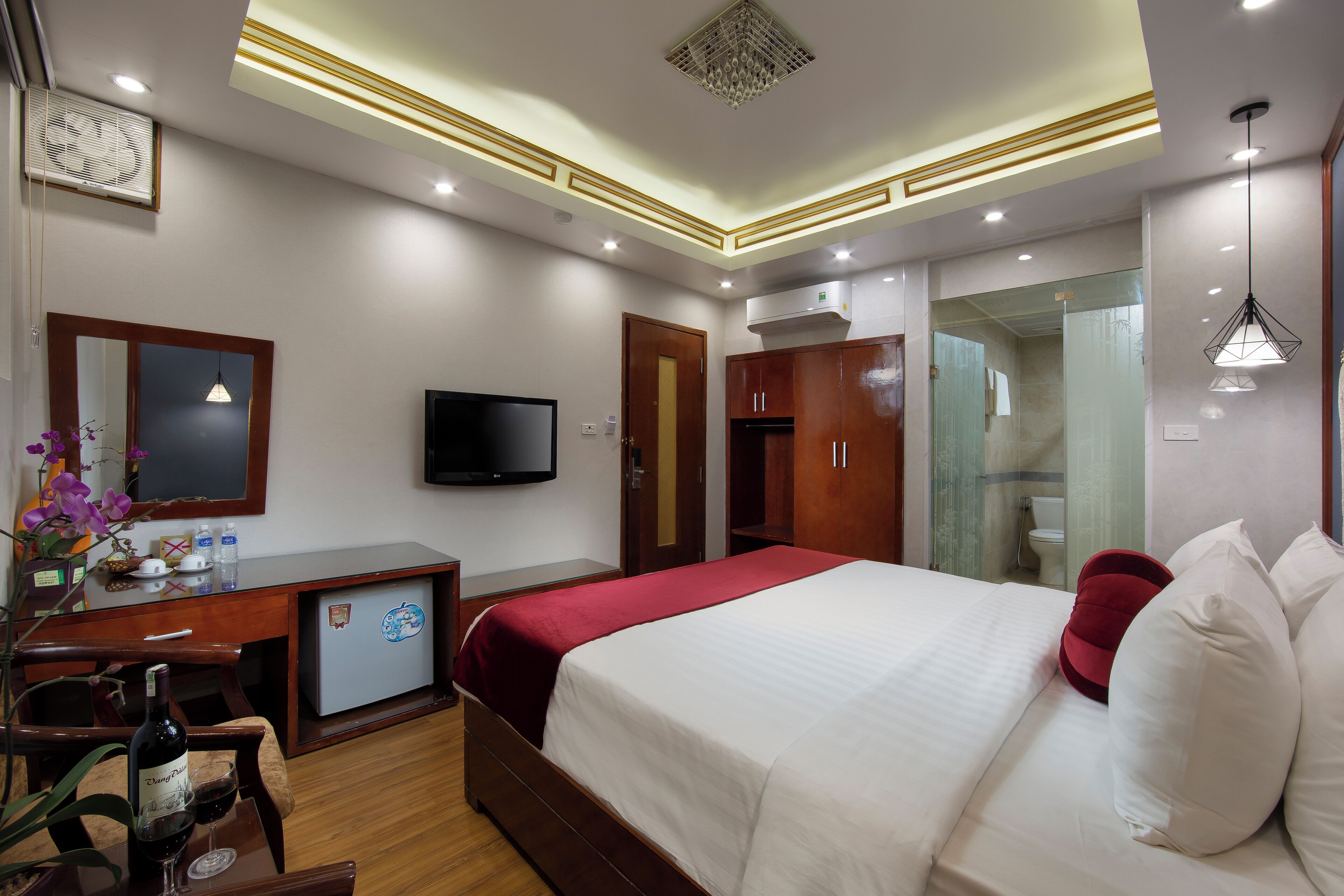 A hotel room with a bed, a desk with a computer, a TV, and a minibar.