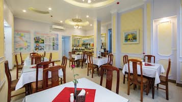 A hotel dining area with multiple tables and chairs, a map on the wall, and a flower on the table.
