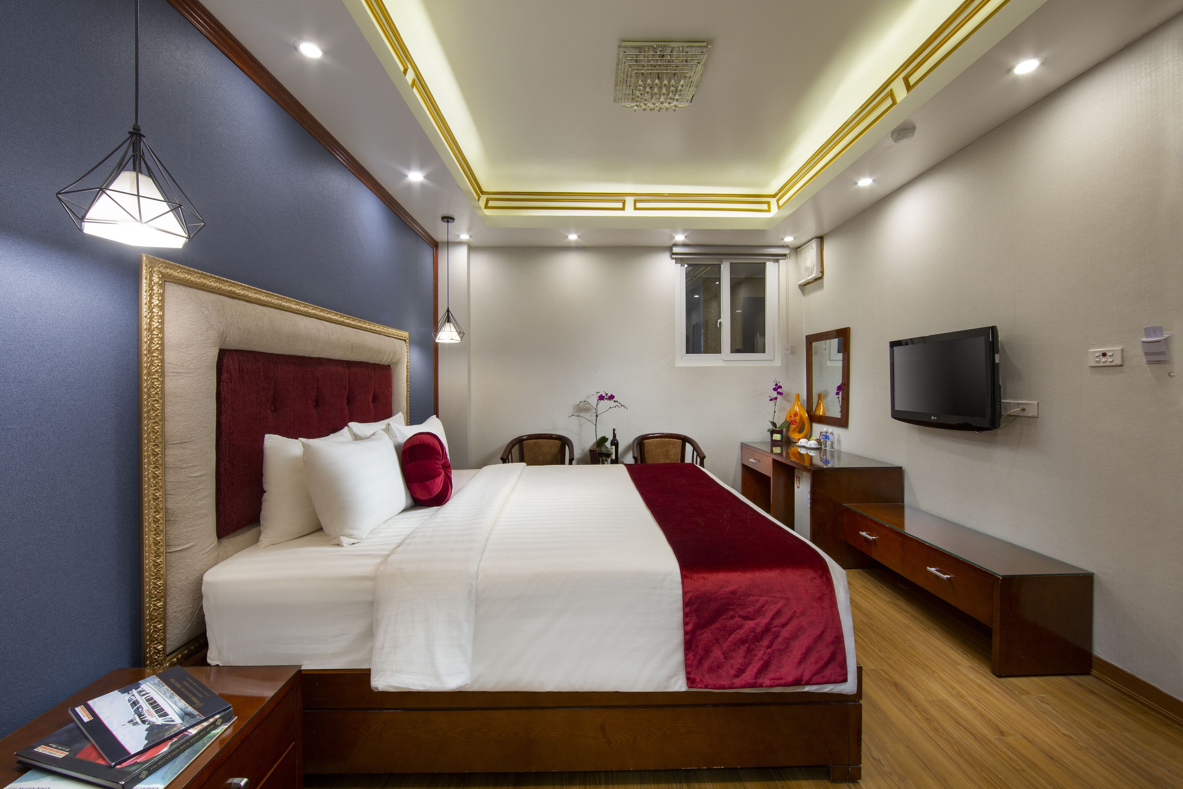 A hotel room with a large bed, a desk with a flat-screen TV, a dresser, and a window.
