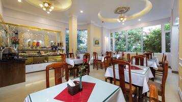 A restaurant with multiple tables and chairs, a buffet area, and large windows offering a view of greenery.