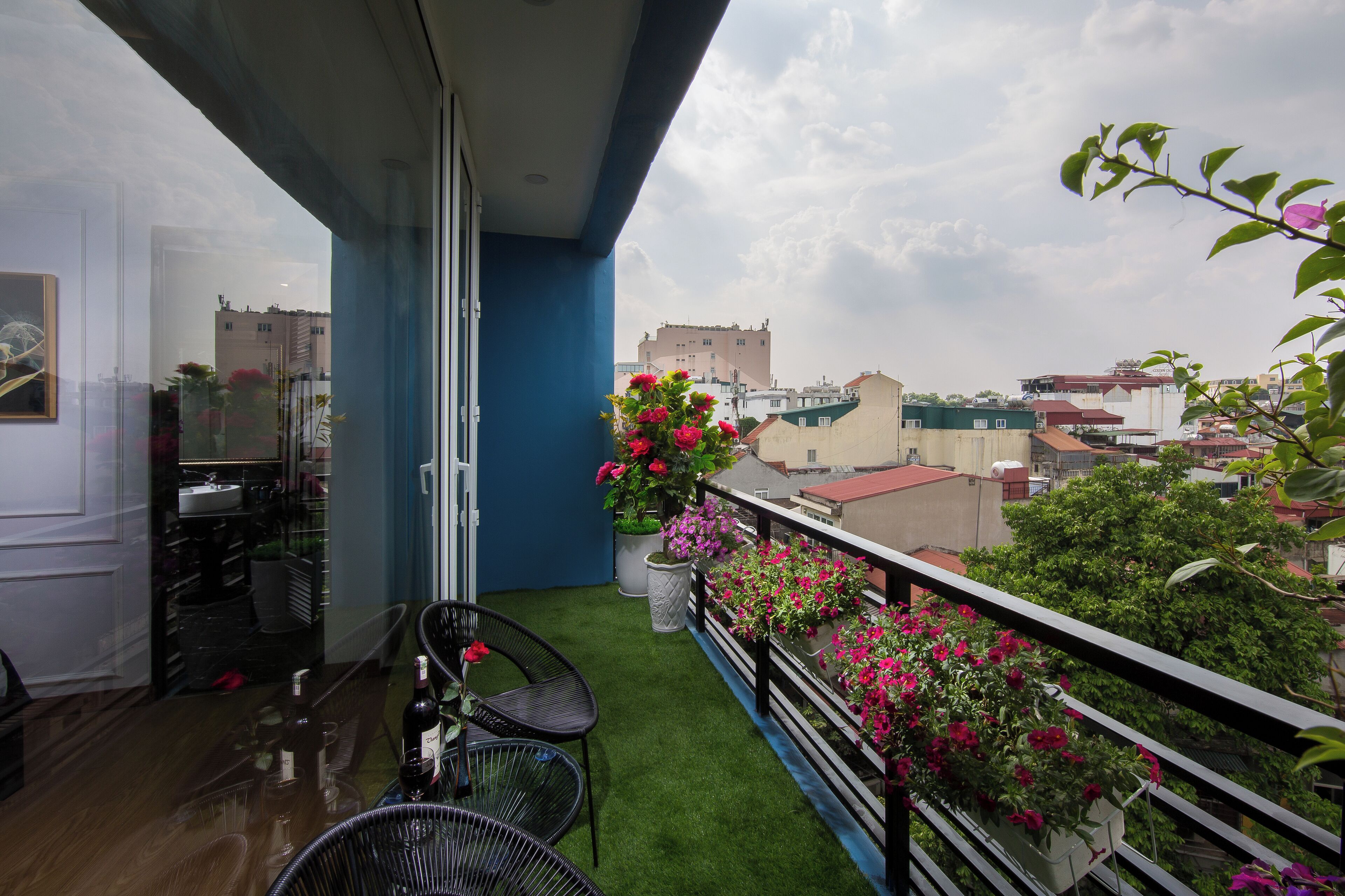 Un balcone con prato sintetico verde, un tavolo da pranzo con sedie e vasi con fiori rosa.