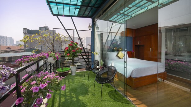 Une chambre moderne avec une cloison en verre, un lit et un petit balcon agrémenté de plantes et de fleurs en pot.