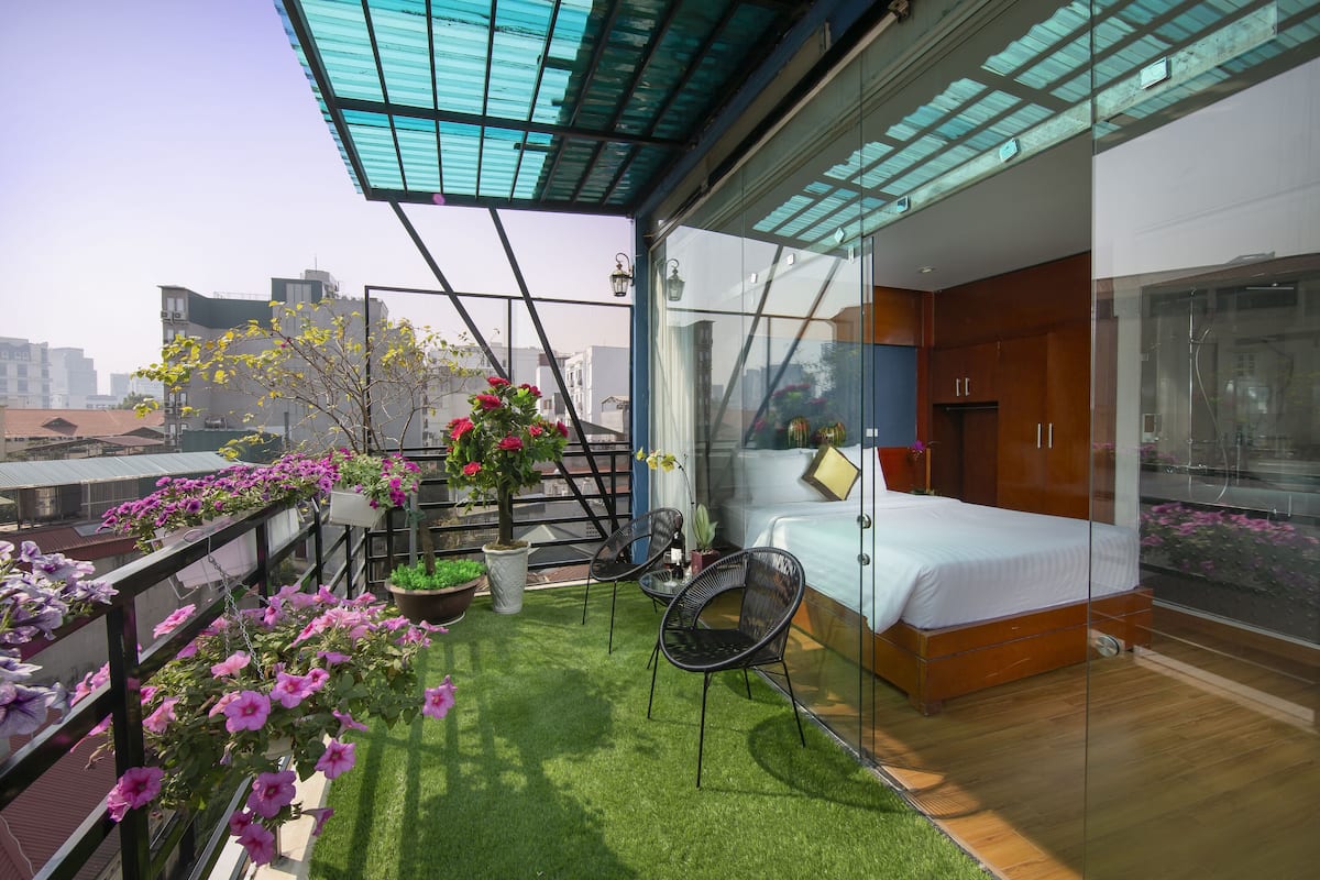 Une chambre moderne avec une cloison en verre, un lit et un petit balcon agrémenté de plantes et de fleurs en pot.