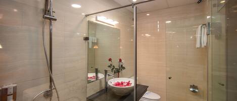 A modern bathroom with a glass-enclosed shower, a white sink with a rose vase, and a toilet.