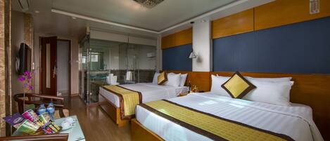 Quarto de hotel com duas camas, área de estar com mesa e cadeiras, vista para o banheiro e cozinha.
