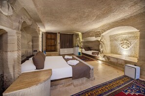 A stone-walled bedroom with a bed, a bench, and a small table. - Kayatas Cave Suites (Nevsehir)