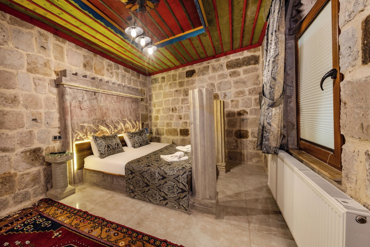 A stone-walled bedroom with a bed, a radiator, and a patterned rug.