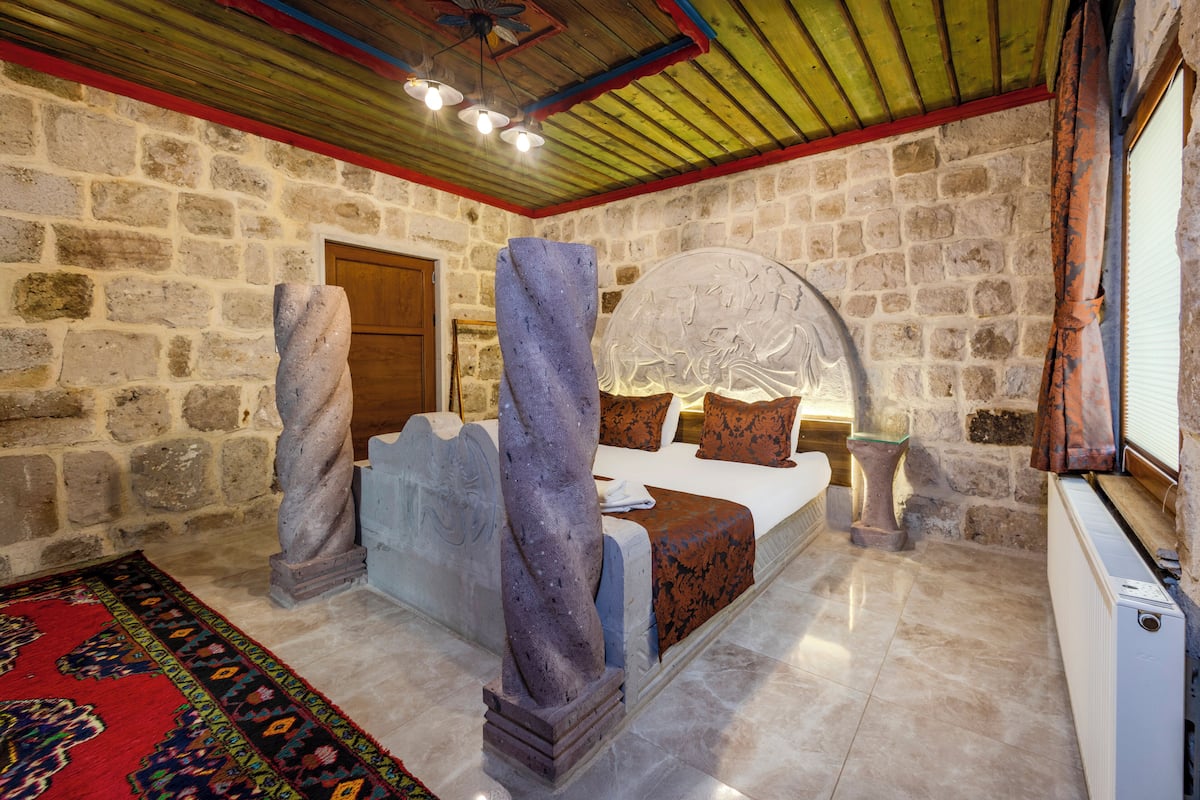 A stone-walled bedroom with a bed, a stone pillar, and a decorative ceiling.