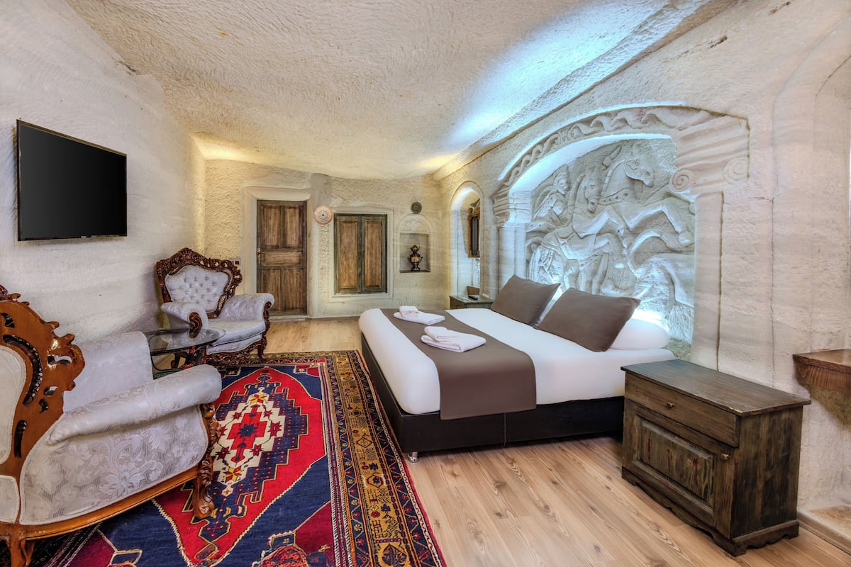 A bedroom with a bed, a wooden nightstand, a chair, a television, and a decorative wall.