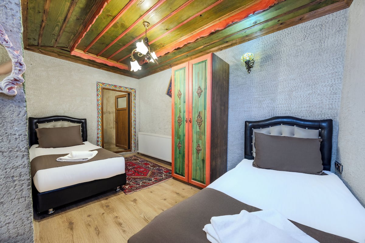 A bedroom with two beds, wooden flooring, a red and green wardrobe, and a patterned rug.