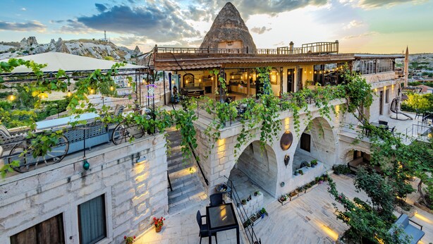 Un bâtiment traditionnel en pierre, doté d’un toit conique, d’une terrasse avec des sièges et offrant une vue sur le paysage environnant.
