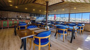 Un restaurant avec des tables en bois et des chaises à coussins bleus, un plafond en bois et de grandes fenêtres donnant sur un paysage rocheux.