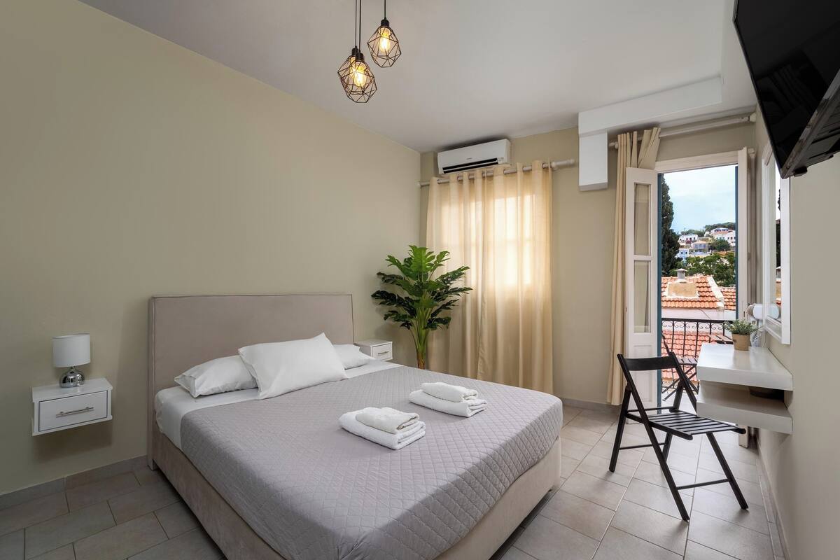 Quarto bem arrumado com cama, mesa de cabeceira, luminária e vista para a varanda.