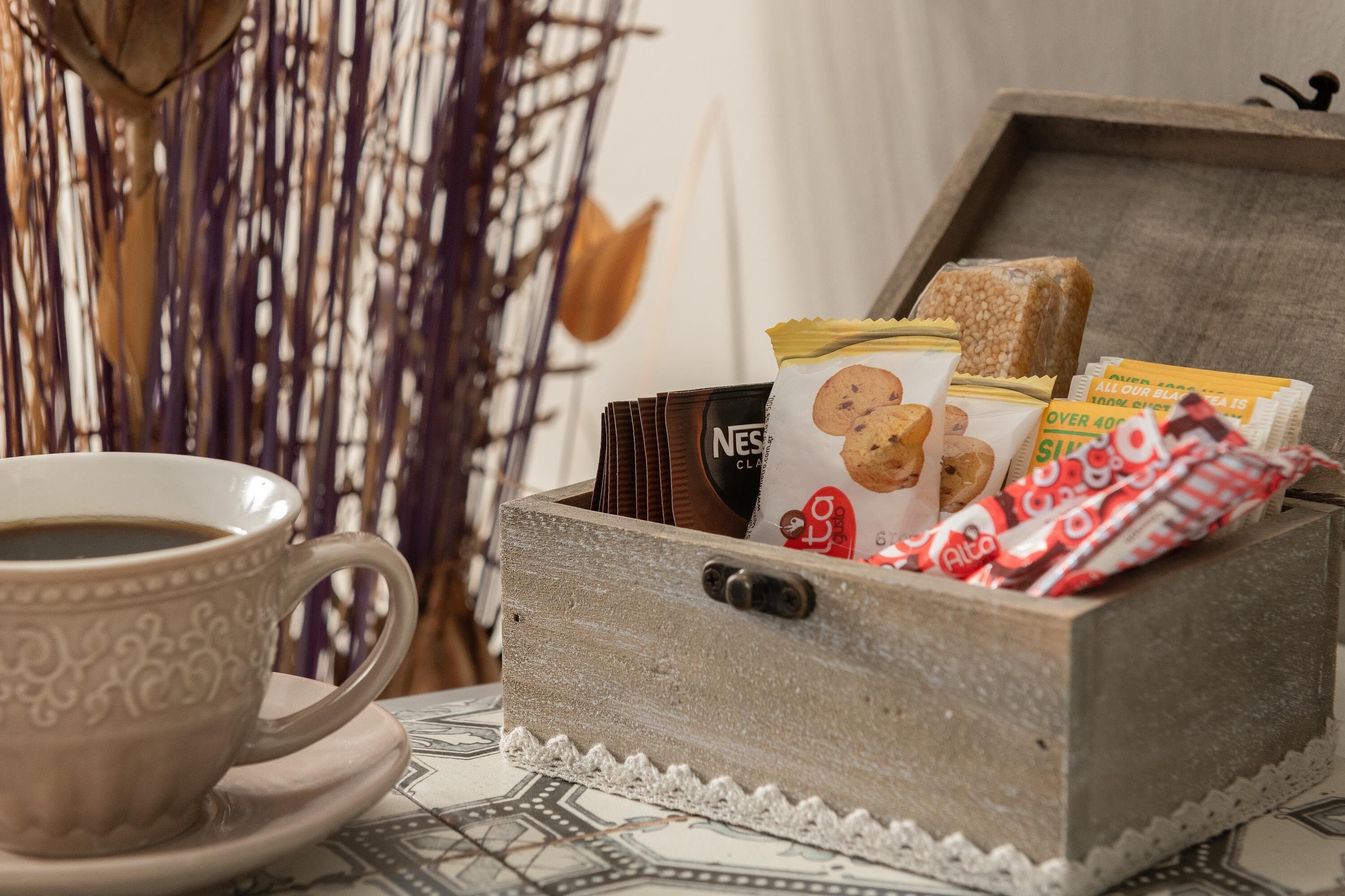 A wooden box containing a coffee cup, a Nescafé Dolce Gusto coffee pod, a pack of cookies, and a bar of chocolate.