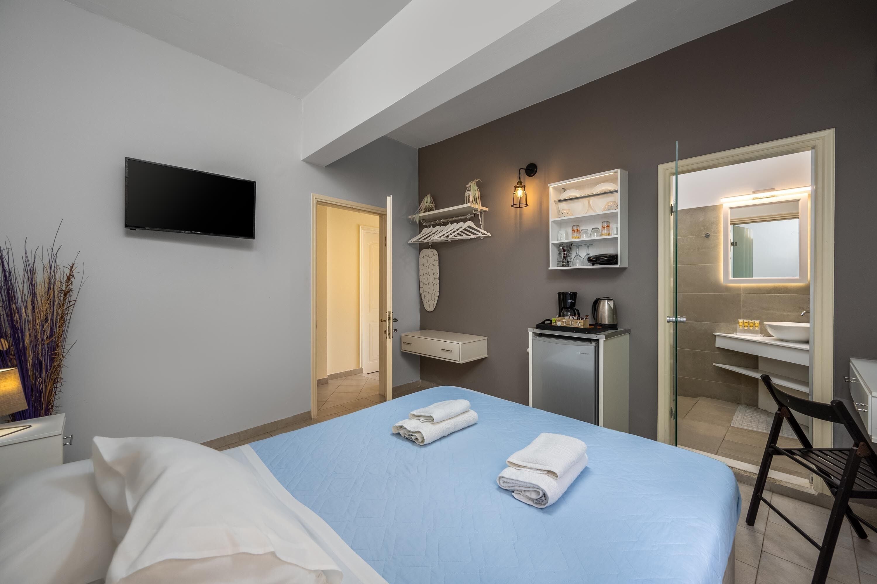 Een moderne hotelkamer met een bed, een televisie, een bureau met stoel, een kitchenette en een badkamer met spiegel.
