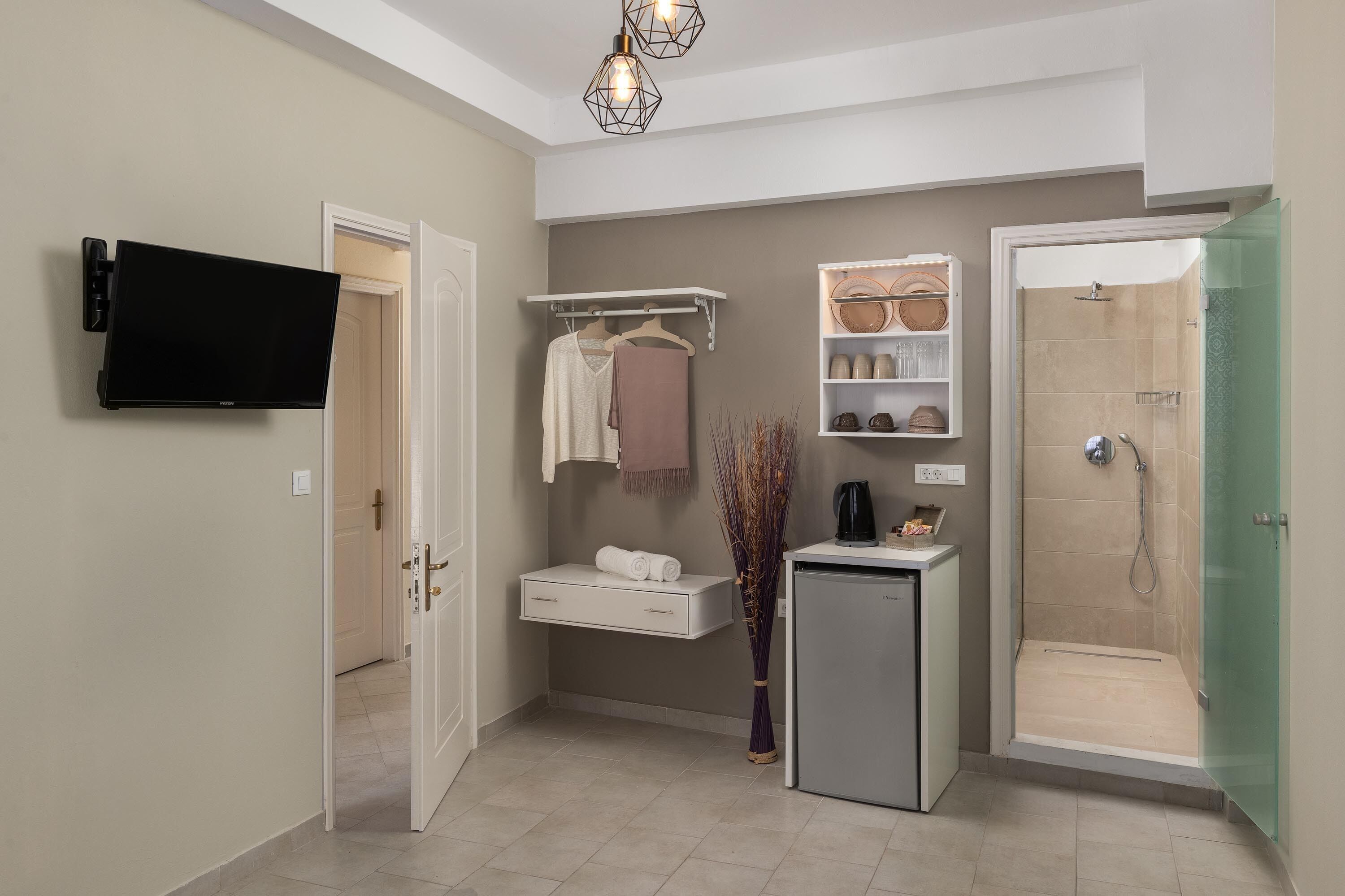 A modern bathroom with a shower, a TV mounted on the wall, a towel rack, and a small cabinet.
