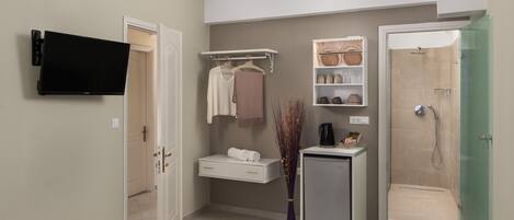 A modern bathroom with a shower, a TV mounted on the wall, a towel rack, and a small cabinet.