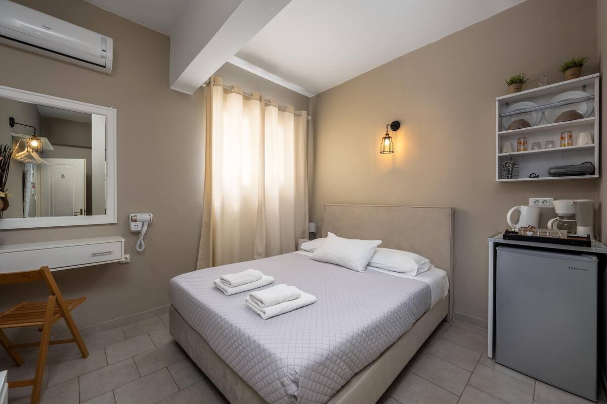 Quarto bem organizado com cama, mesa de cabeceira e uma pequena cozinha compacta.