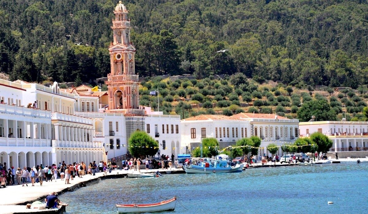 A coastal town with a prominent clock tower, a marina with boats, and a crowd of people.
