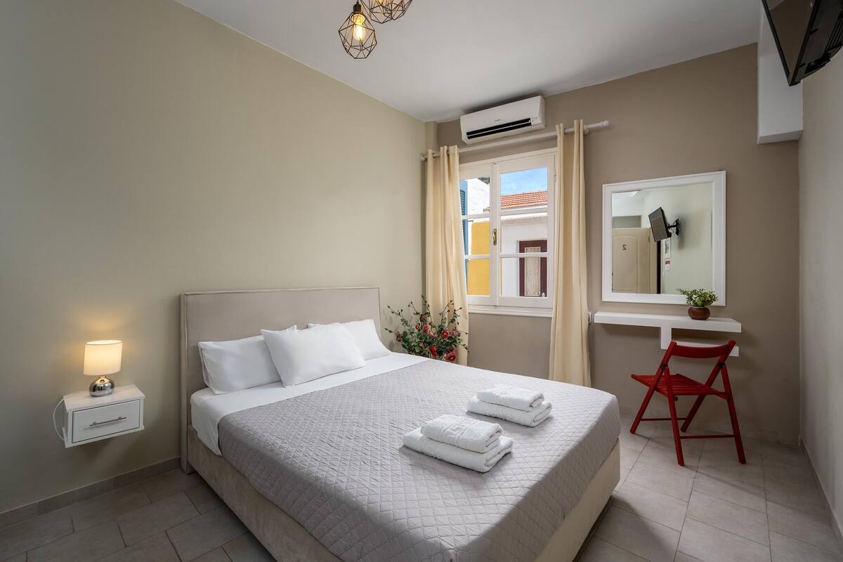 Quarto bem arrumado com cama, mesa de cabeceira e escrivaninha com cadeira.