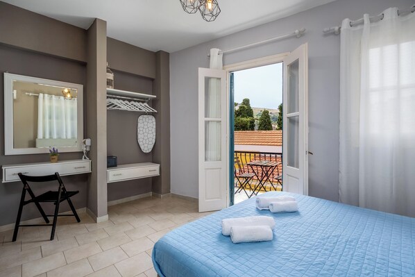 Un dormitorio con cama, escritorio, silla, espejo y balcón con vistas.
