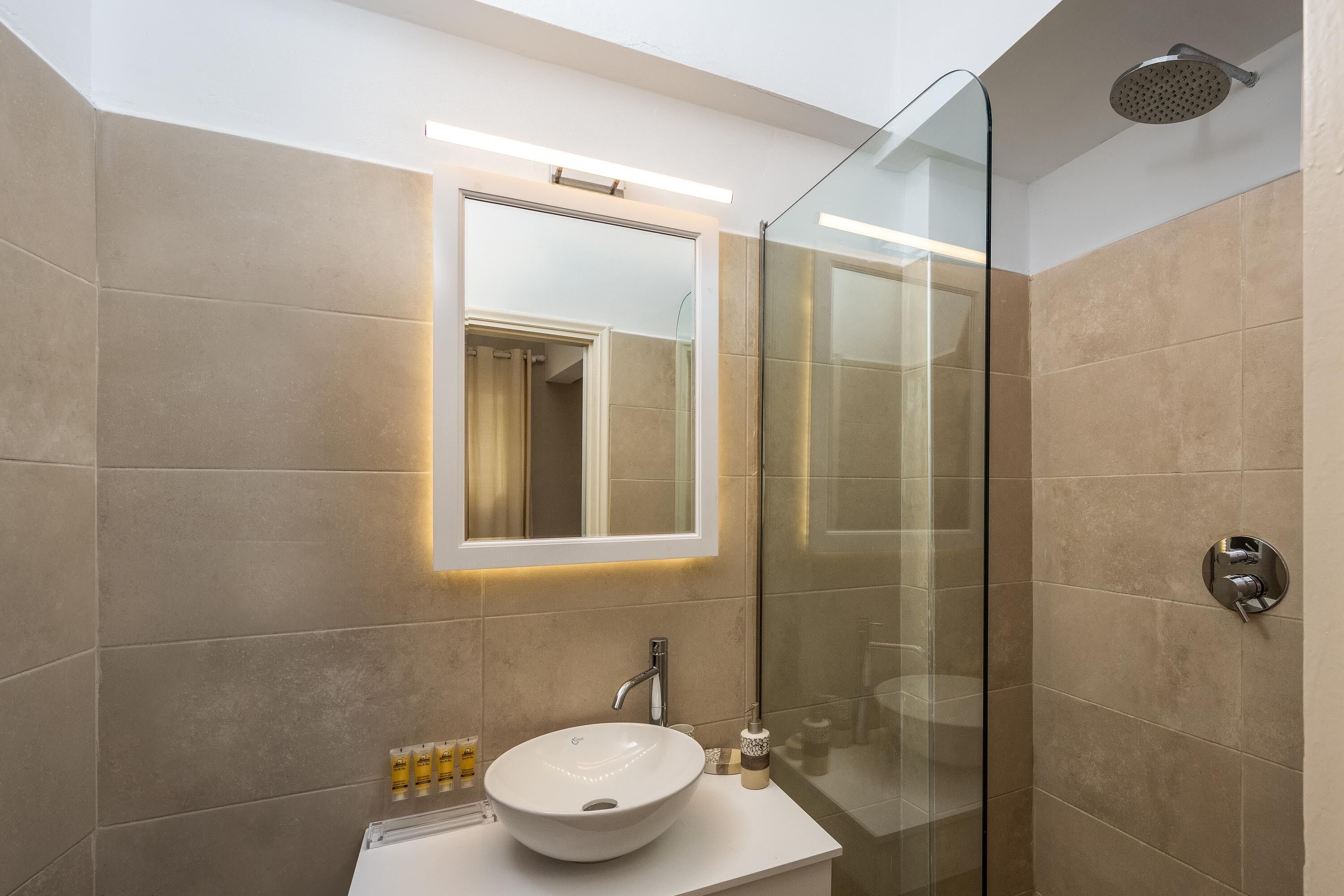 Un baño moderno con cabina de ducha de vidrio, un lavamanos blanco e iluminación integrada en un espejo.