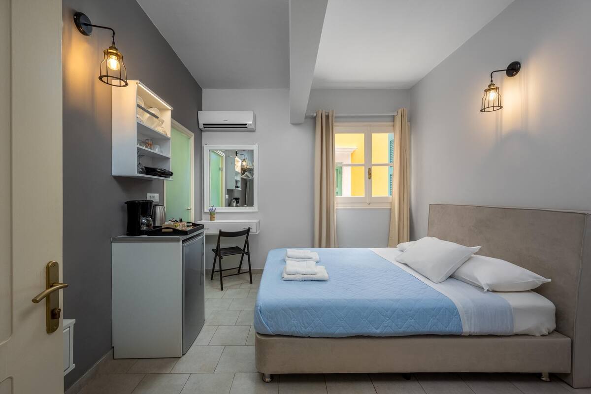 Quarto de hotel com cama, escrivaninha e cozinha compacta.