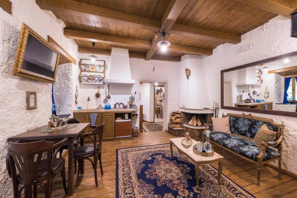 A cozy living room with a wooden ceiling, a dining area with a table and chairs, and a sofa with a floral upholstery.