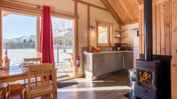 Een gezellig blokhut met houten inrichting, een keukenhoek en een eethoek met uitzicht op een besneeuwd landschap.