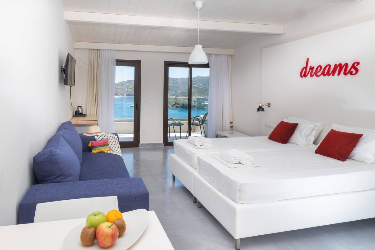Une chambre d’hôtel moderne avec un lit, un canapé, une table à manger avec des fruits et un balcon offrant une vue agréable.