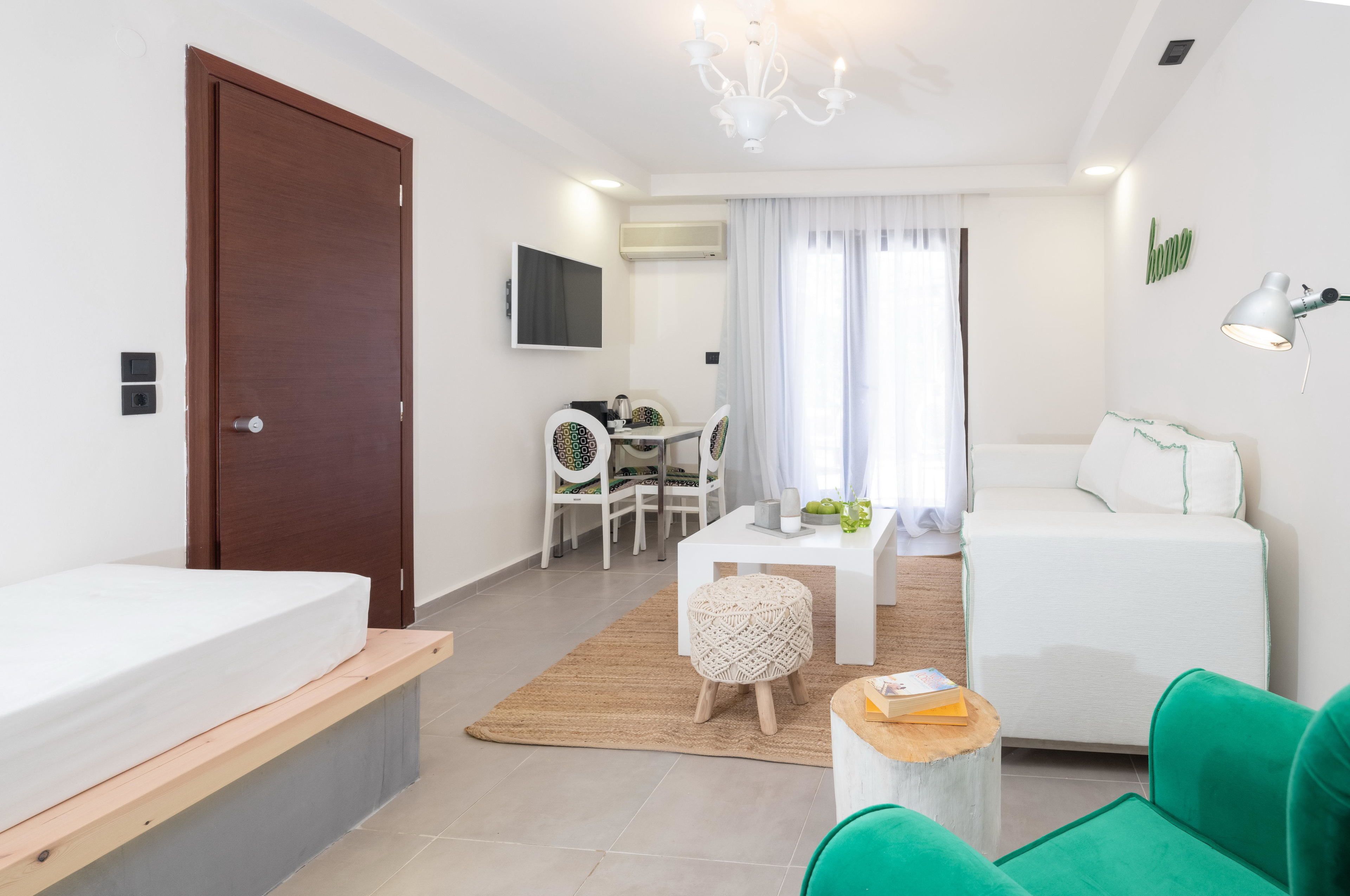 Una habitación de hotel moderna y bien iluminada, con cama, sofá, zona de comedor con sillas, una mesita y televisor montado en la pared.