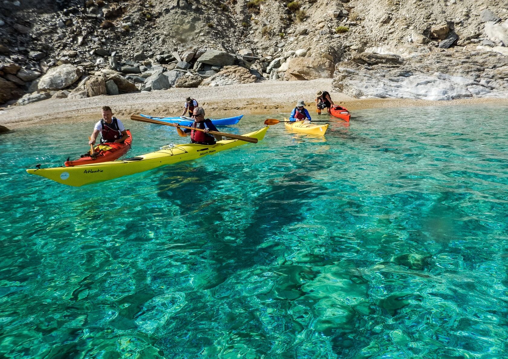 Kayakers in clear water near a rocky shore.