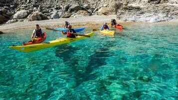 Kayakers in clear water near a rocky shore.