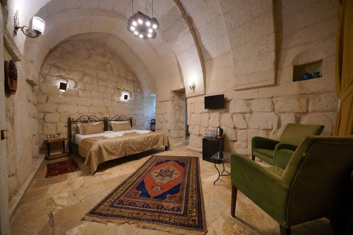 A room with a stone wall, a bed, a green chair, and a rug.